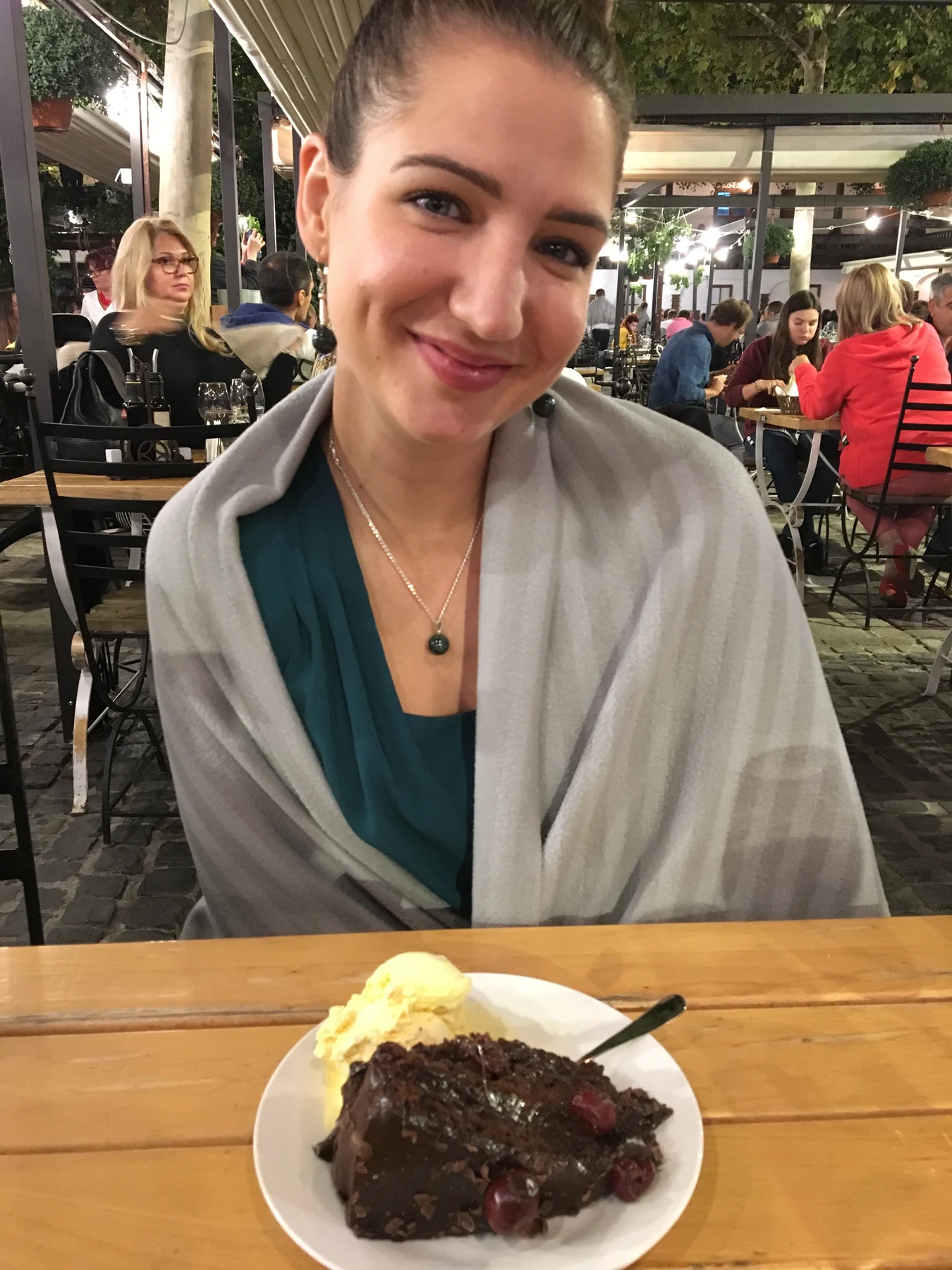 A smiling woman seated at a table with a chocolate dessert.